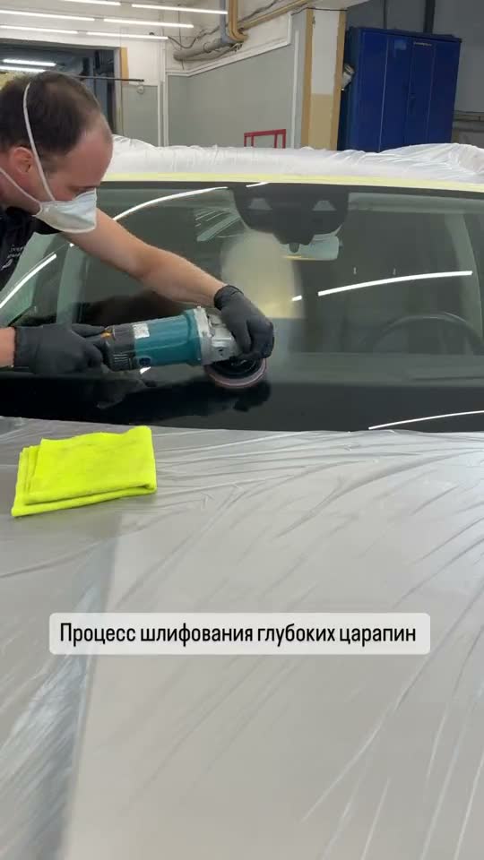 Мастер шлифует лобовое стекло машинкой, кузов закрыт плёнкой