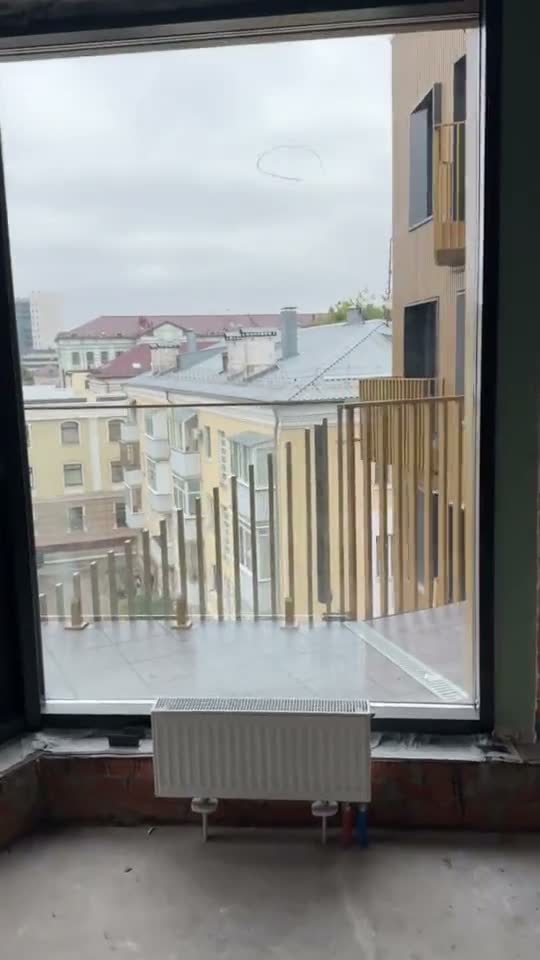 Окно квартиры с видом на крыши соседних домов, под окном радиатор