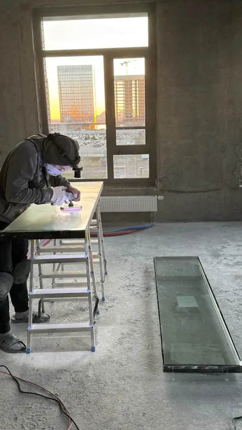 Мастер в респираторе полирует стеклопакет на столе