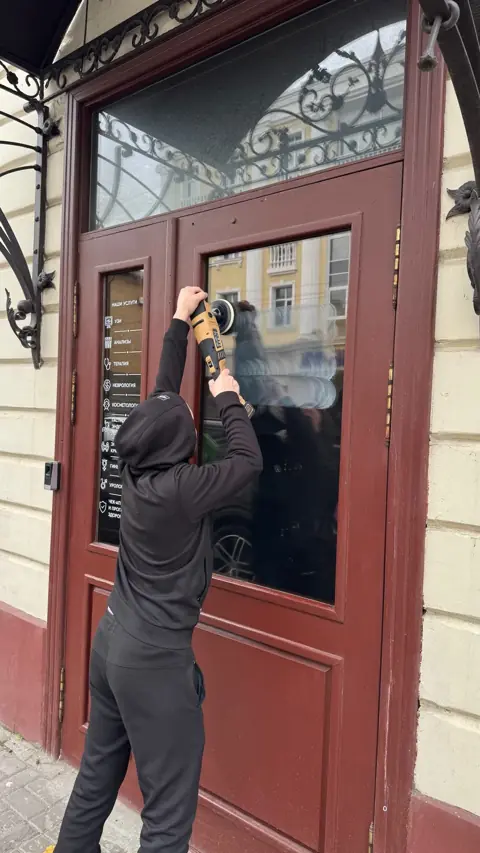 Мастер шлифует стекло входной двери с ковкой