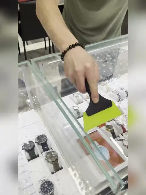 Мастер очищает стекло часовой витрины скребком